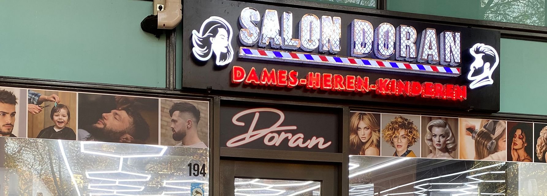 De gevel van Salon Doran met lichtreclame en portretten in de etalage